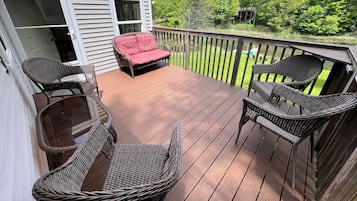 Relax on the deck with wicker chairs and a cushioned bench, surrounded by a lush landscape.