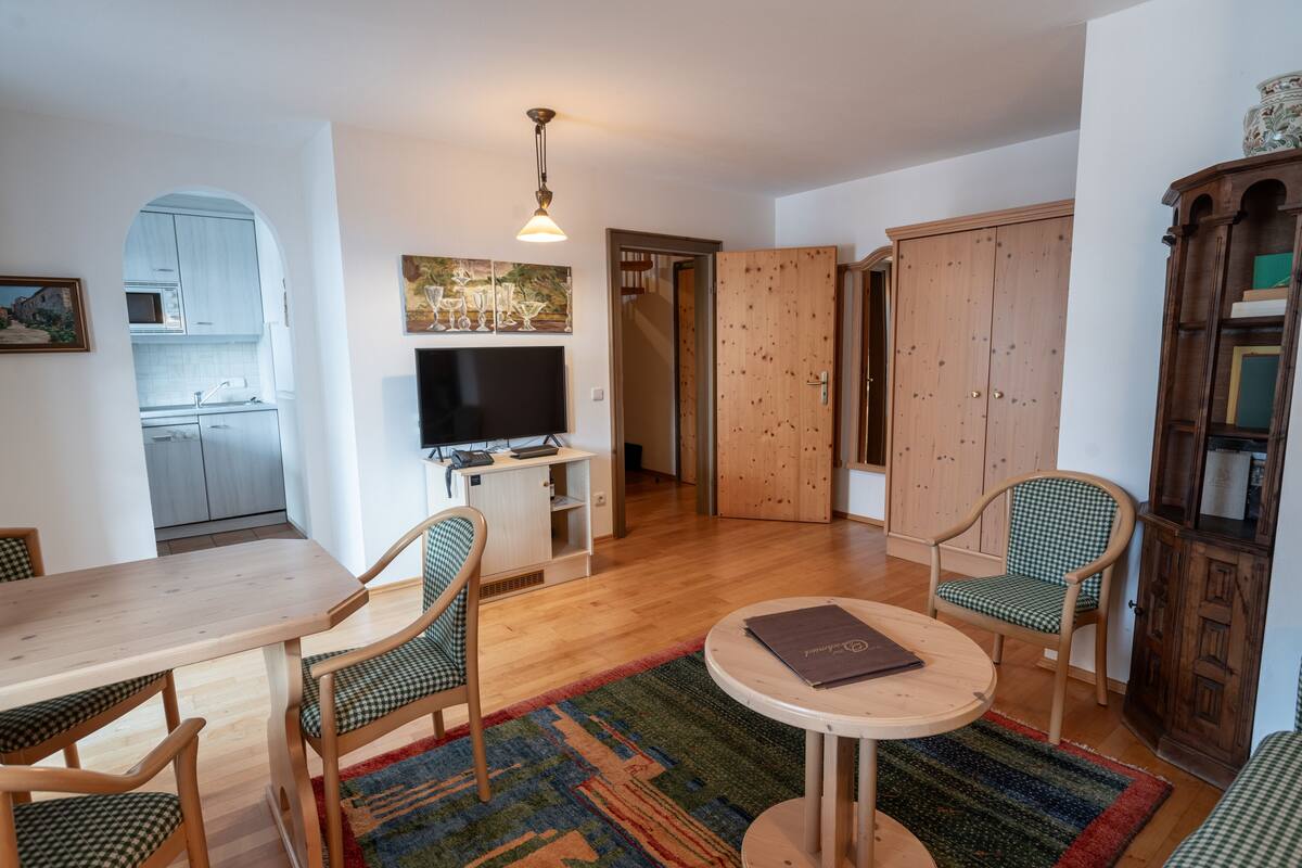 Ett vardagsrum med ett matbord i trä, två stolar, en tv och en bokhylla.