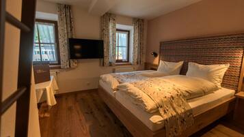 Ein Schlafzimmer mit einem hölzernen Bett, zwei mit Vorhängen versehenen Fenstern, einem Flachbildfernseher und einem Nachttisch.