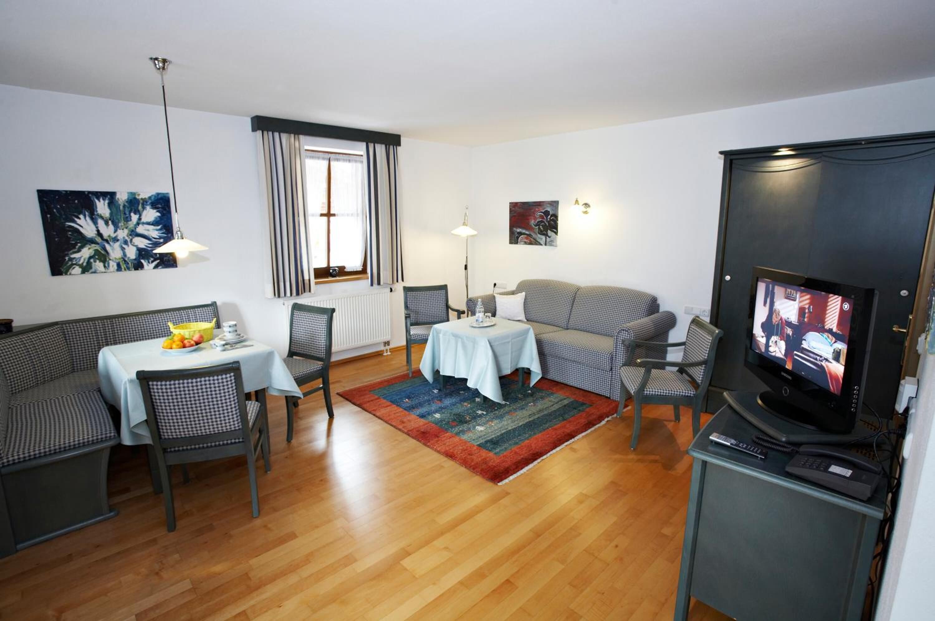 A living room with a sofa, a dining table with chairs, a TV, and artwork on the walls.