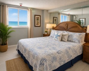 A bedroom with a bed, a nightstand, a lamp, a potted plant, and a view of the ocean. - Sand Dollar Breathtaking Direct Oceanfront Views, New Pool and Beach Access Open (Daytona Beach Shores)