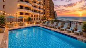 A hotel pool with a sunset view, lounge chairs, and a sign indicating the pool's depth. - Sand Dollar Breathtaking Direct Oceanfront Views, New Pool and Beach Access Open (Daytona Beach Shores)