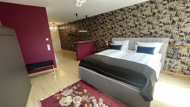 A modern bedroom with a large bed, a desk, and a patterned wall. - Design Apartment Catch Me If You Can (Freiburg im Breisgau)