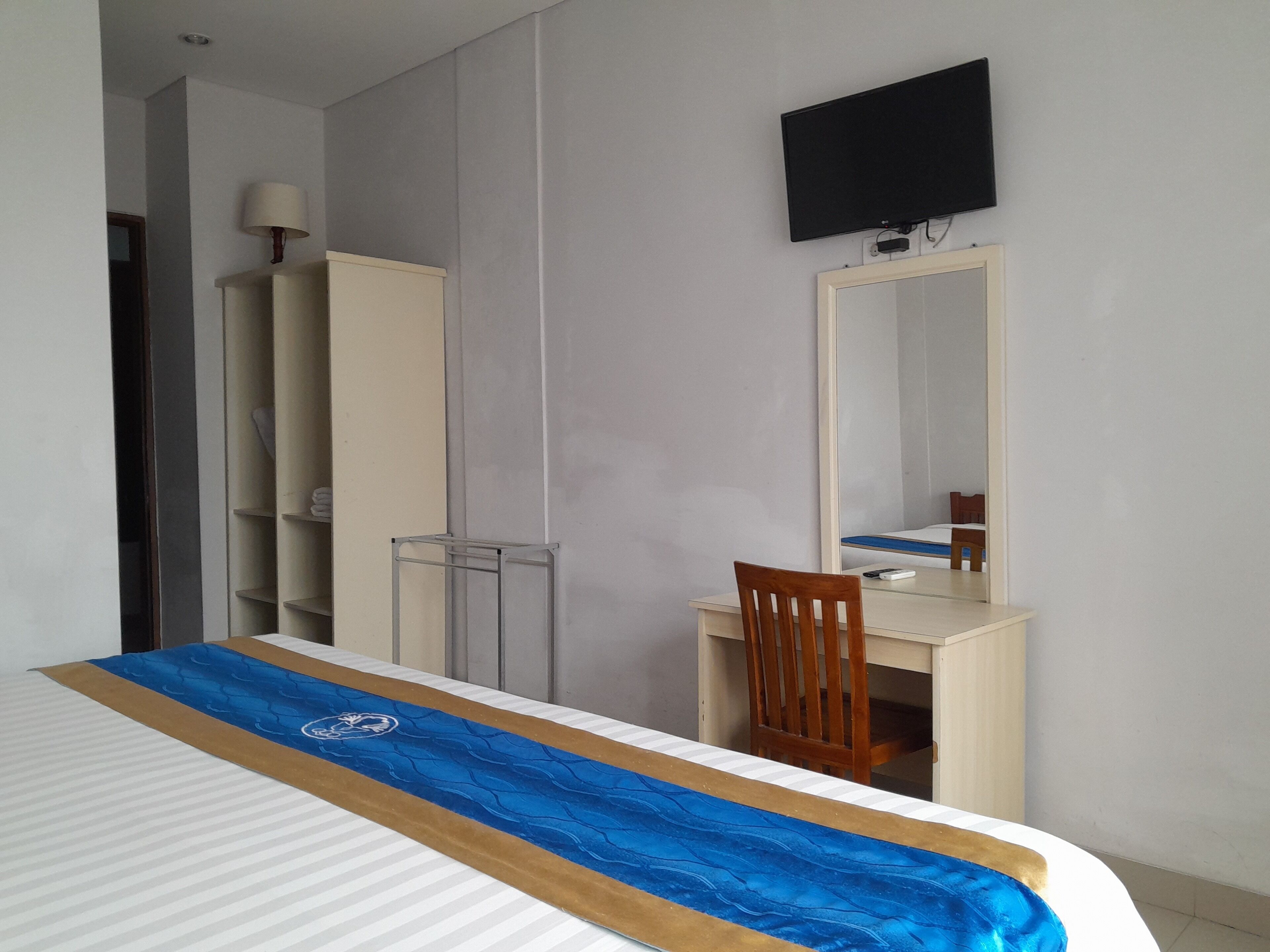 A hotel room with a bed, a desk, a chair, a TV mounted on the wall, and a wardrobe.