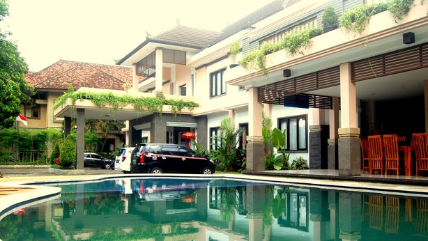 A swimming pool with a reflection of a building and parked cars. - Dhyanapura City Hotel (Mengwi)