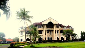 A large, historic building with a symmetrical facade, multiple arches, and a central entrance. - Dhyanapura City Hotel (Mengwi)