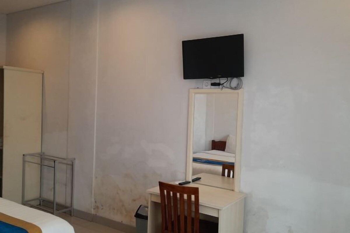 Habitación de hotel con una cama, un escritorio con una silla, un televisor montado en la pared y una mesita con otra silla.