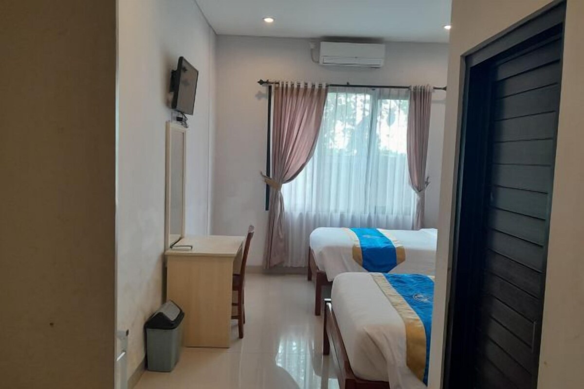 A hotel room with a bed, a desk, a chair, a TV mounted on the wall, and a window with curtains.