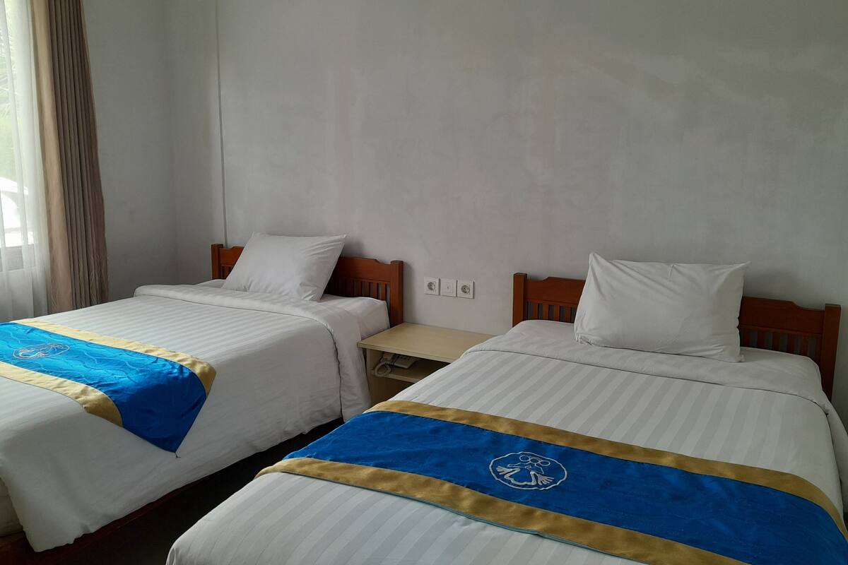 A hotel room with two beds, each with a blue and gold bedspread and white pillows.