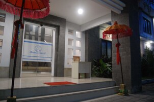 Entrada de un hotel con mostrador de recepción, una alfombra roja y dos paraguas rojos.