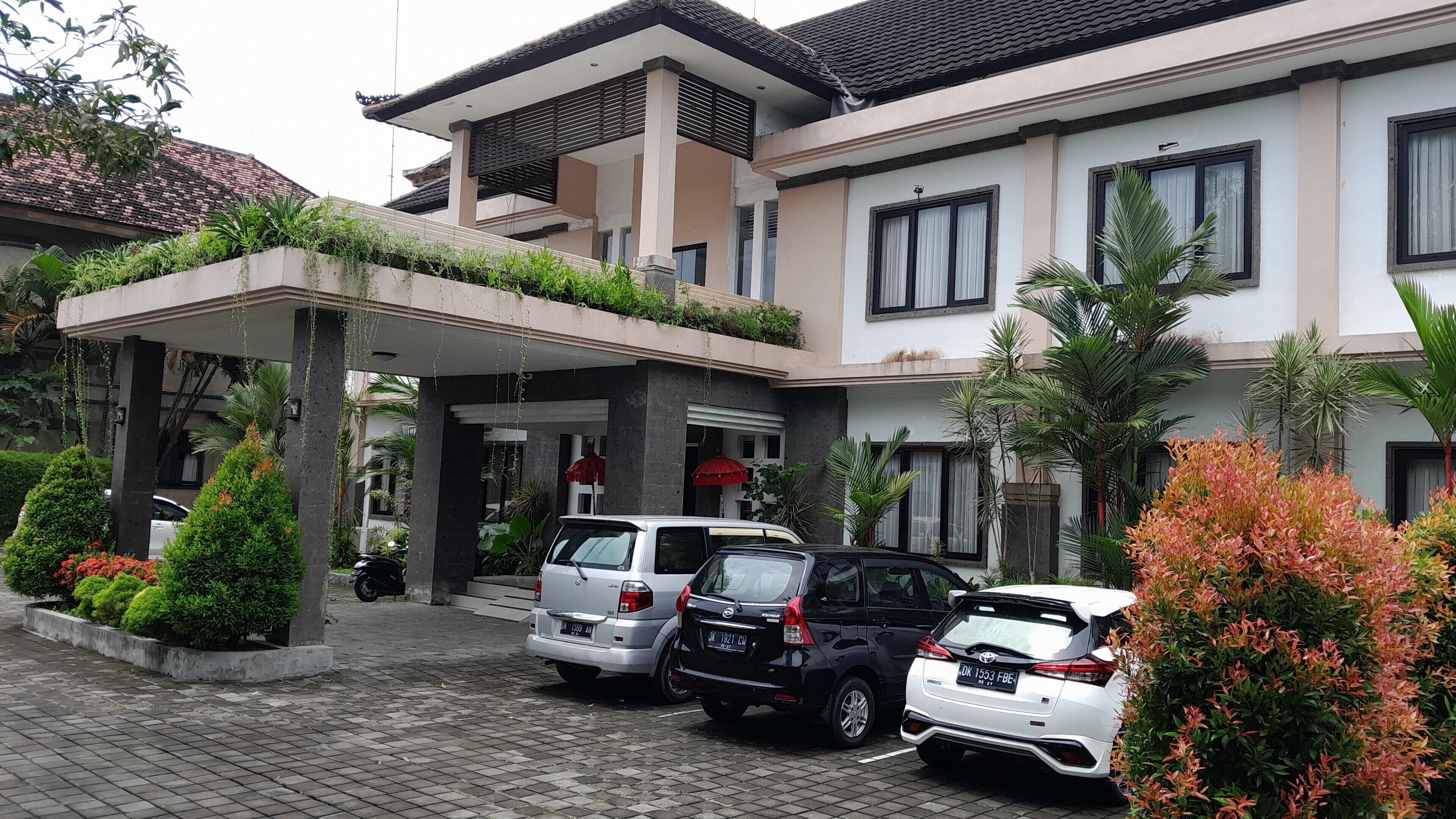 A two-story building with a covered entrance, parked cars, and lush greenery.