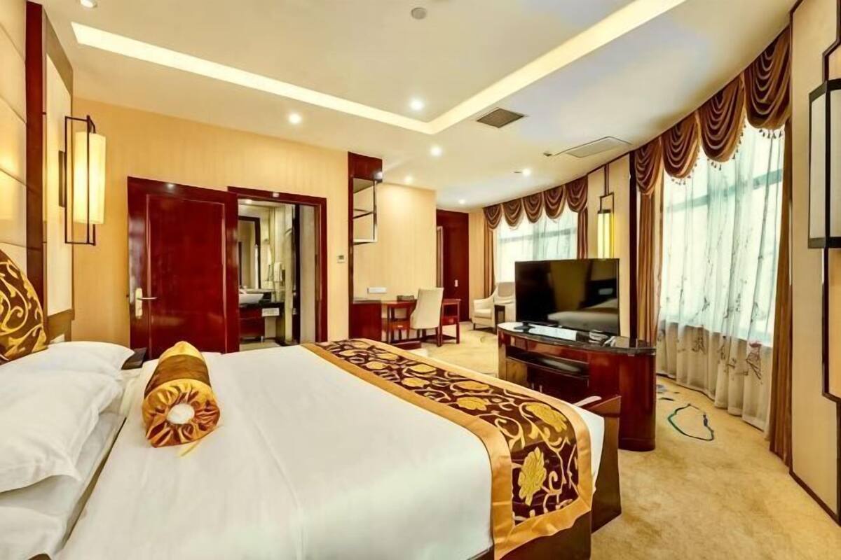 A hotel room with a large bed, a desk with a computer, a TV, and a door leading to a bathroom.