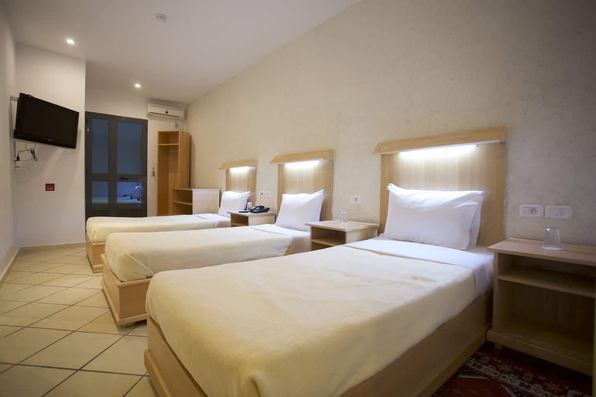 A hotel room with three single beds, a TV mounted on the wall, and a wooden wardrobe.