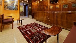 A lobby with a wooden reception desk, a red patterned rug, and a painting of a cityscape. - Hotel Roma Tunis (Tunis)