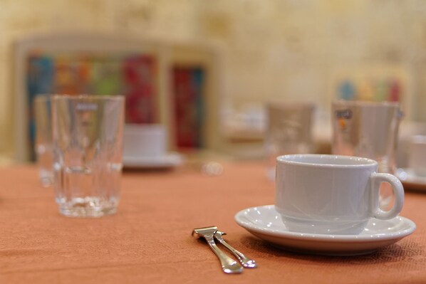 A table with a white cup and saucer, a glass, and a spoon.