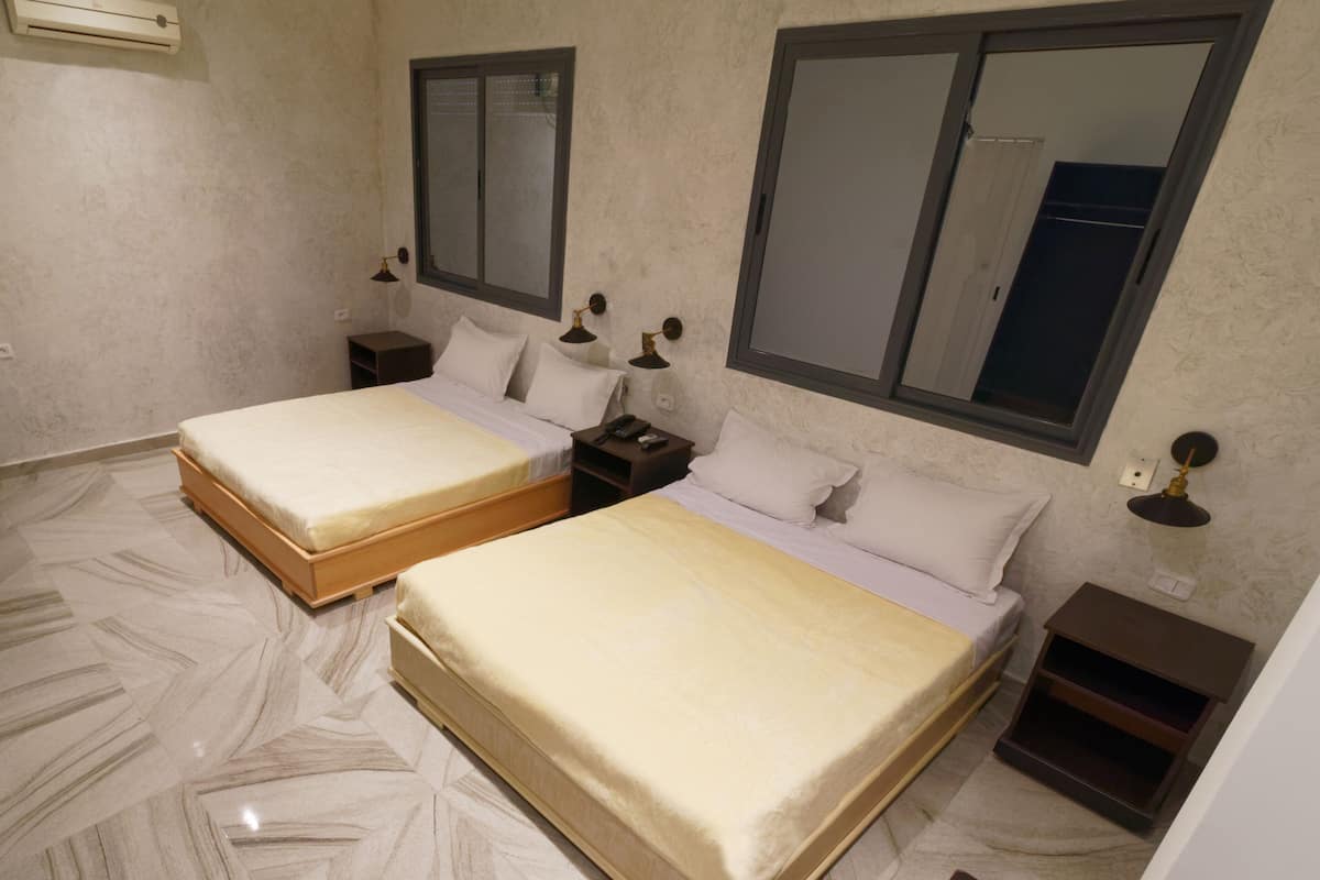A bedroom with two beds, a nightstand, a lamp, and a mirror.
