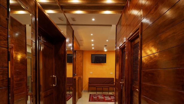 A hallway with wooden paneling, a bench, and a television mounted on the wall. - Hotel Roma Tunis (Tunis)