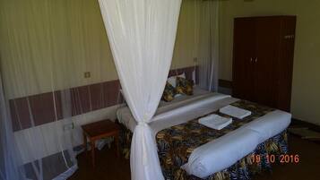 A room with a bed, a wooden nightstand, a wardrobe, and a mosquito net.