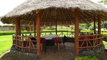 Un espacio de estar al aire libre cubierto, con techo de paja, suelo de piedra y barandillas de madera.