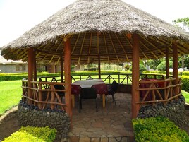 Un espacio de estar al aire libre cubierto, con techo de paja, suelo de piedra y barandillas de madera.