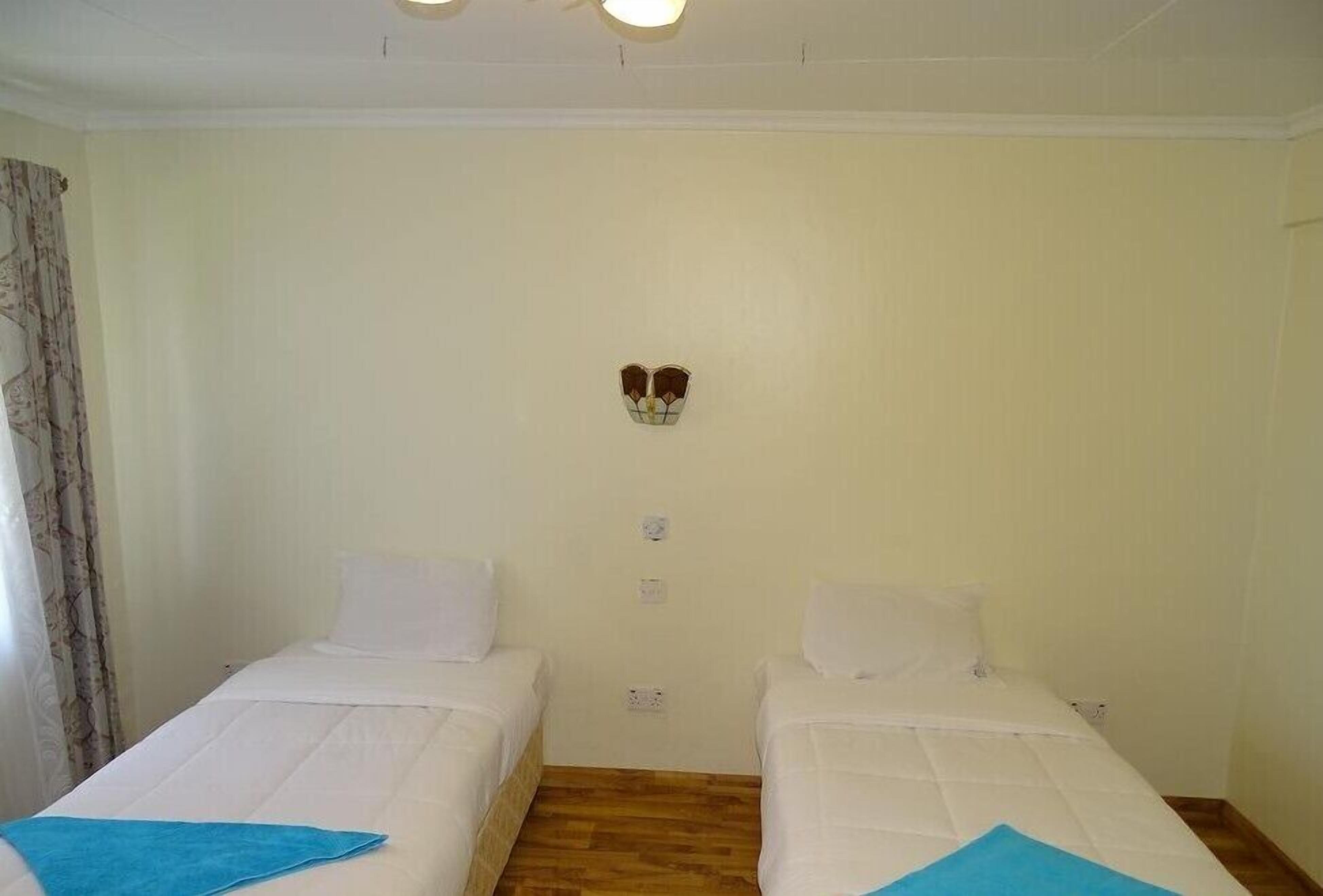 Una habitación con dos camas individuales, una lámpara pequeña en la pared y suelo de madera.