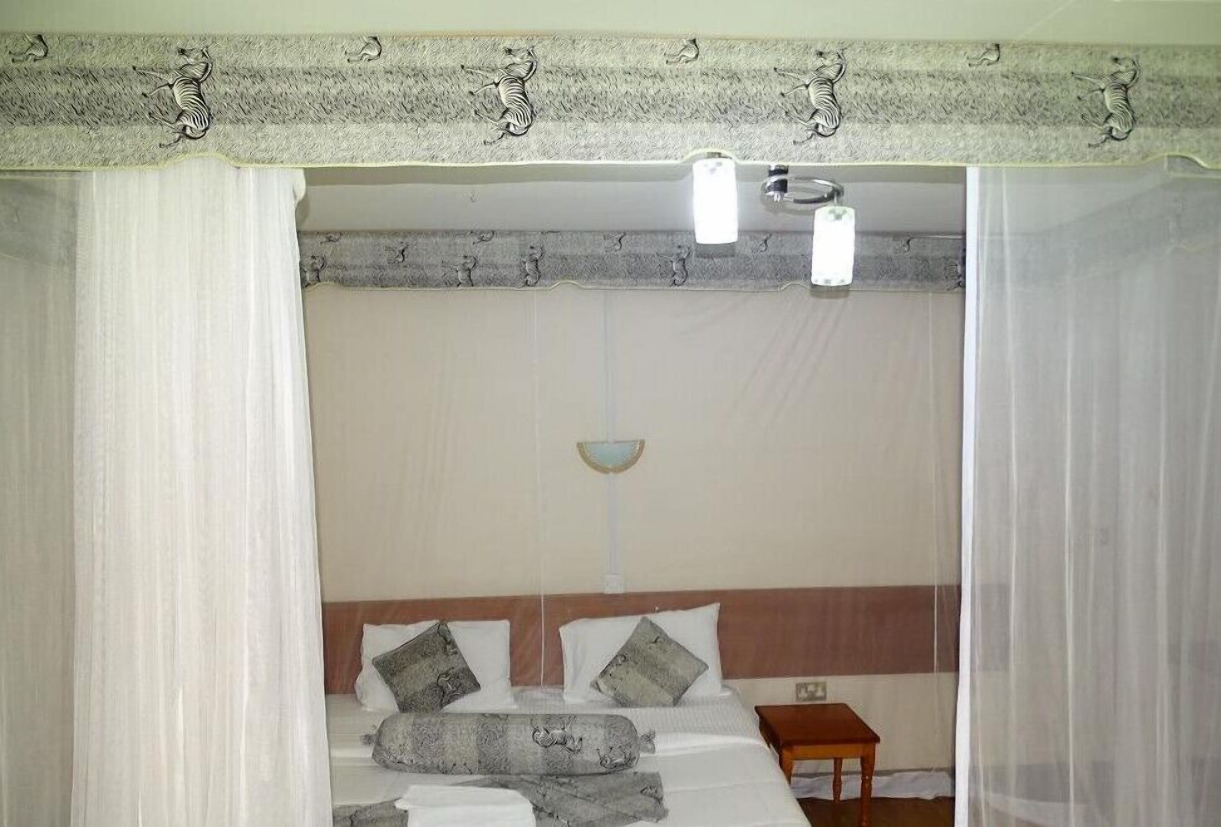 A bedroom with a bed, a small table, and a wall-mounted light fixture.