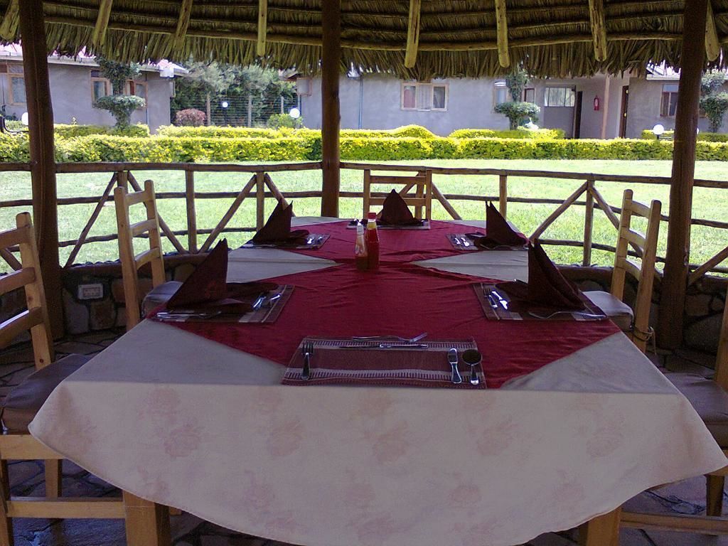 A dining table set for six with a red tablecloth, wooden chairs, and a thatched roof structure.