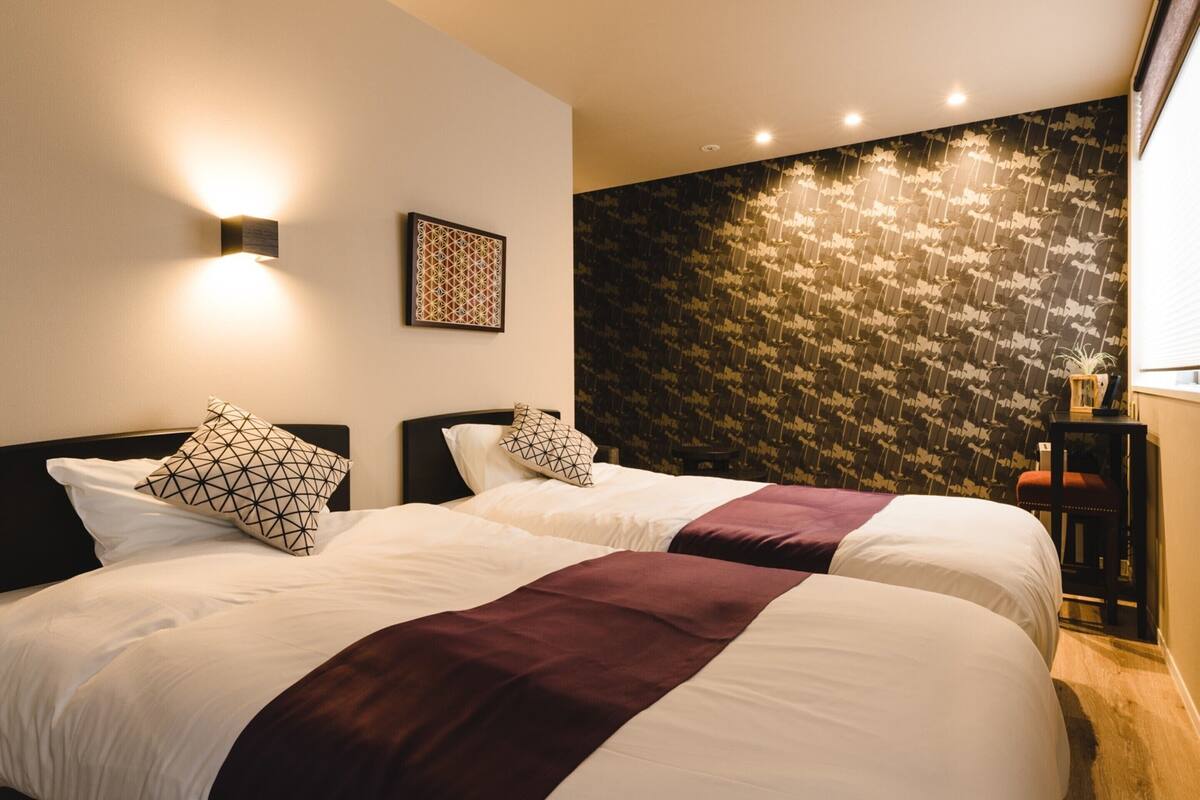 Ein Hotelzimmer mit zwei Betten, einer Wand mit dunklem Muster und einem kleinen Tisch mit einer Pflanze.