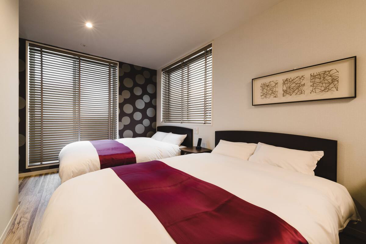Ein Hotelzimmer mit zwei Betten, einem großen Fenster mit Jalousien, einem Wandbild und einer gemusterten Wand.