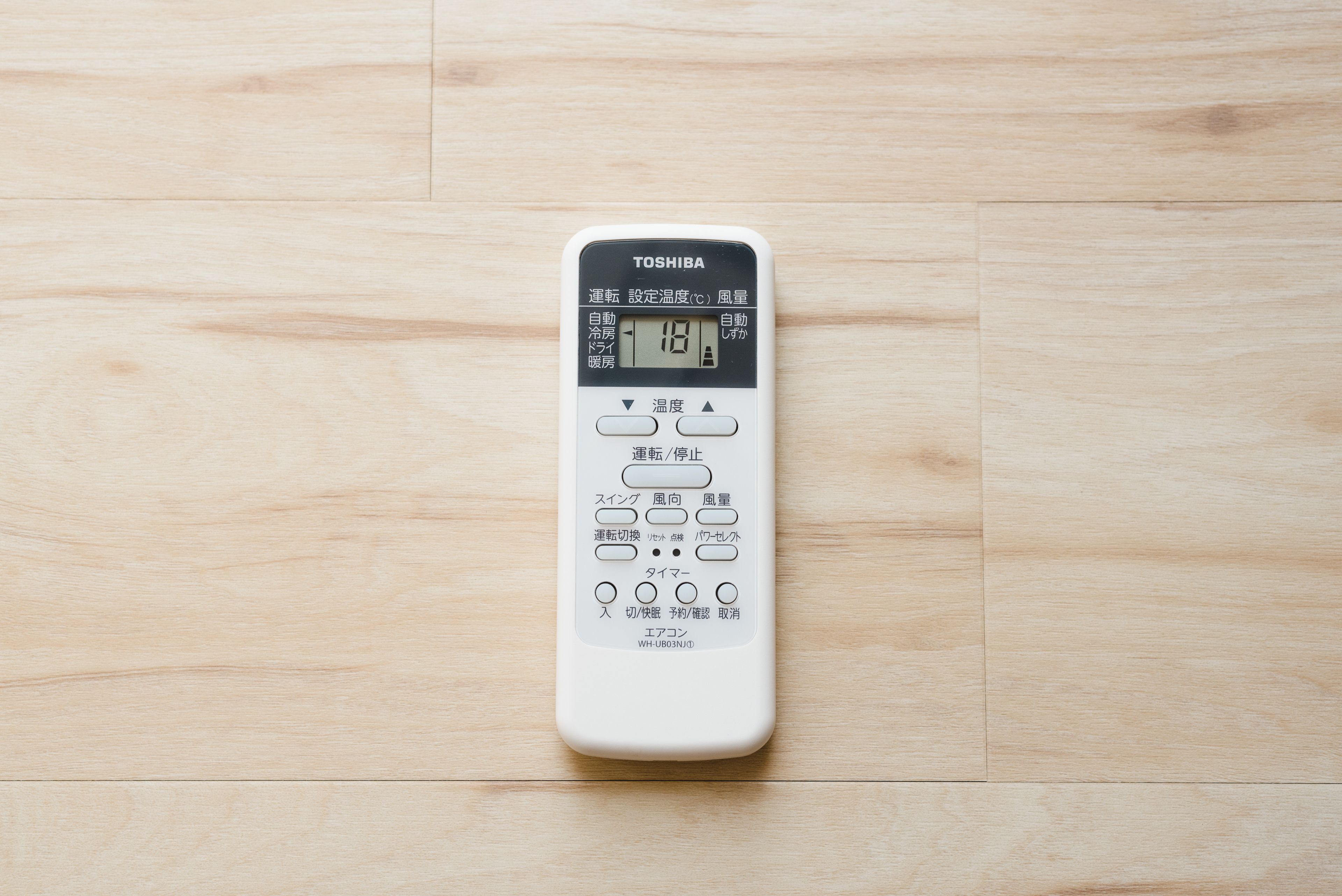 A white Toshiba remote control on a wooden floor.