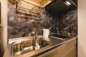 A modern kitchen with a stainless steel sink, a kettle, and a geometric tile backsplash. - Trip Base HAKATAEKIMAE (Fukuoka)