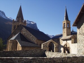 A historic church with a prominent bell tower and a stone facade, set against a mountainous backdrop. - Appart Hotel Panoramic Village (La Grave)