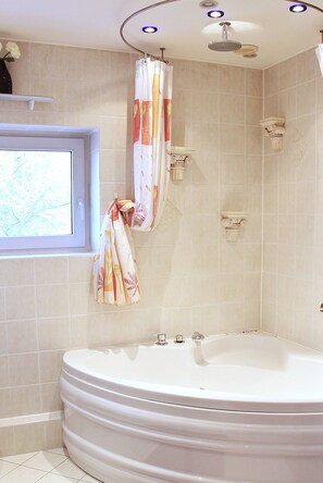 A bathroom with a large bathtub, a showerhead, and a window with a curtain. - Pension Belger (Blankenfelde-Mahlow)