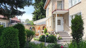 Une maison à deux étages dotée d’un balcon, d’une arche en pierre et d’un jardin bien entretenu.