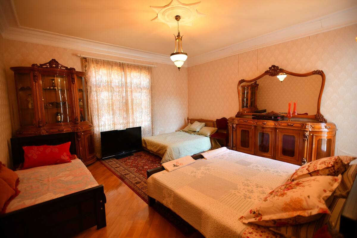A bedroom with a large bed, a television, a wooden cabinet, and a mirror.