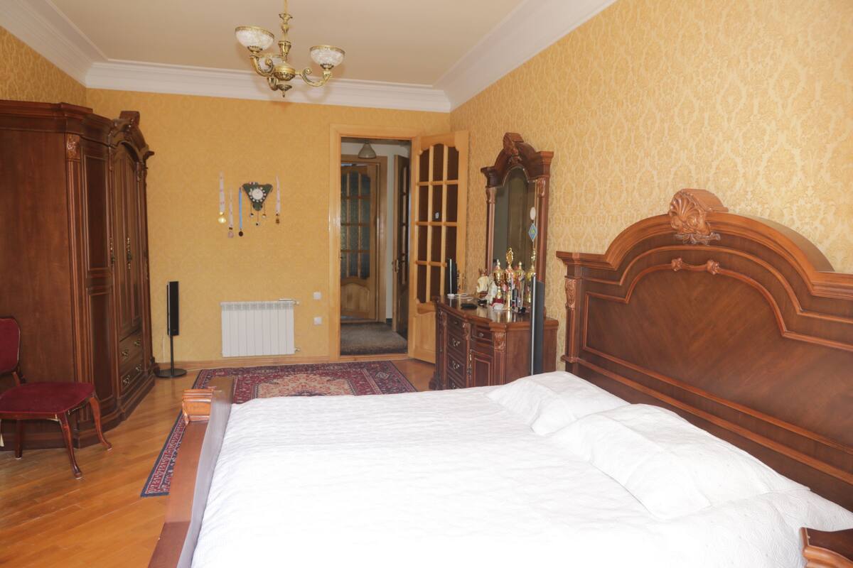 A bedroom with a large bed, wooden wardrobe, and a mirror.