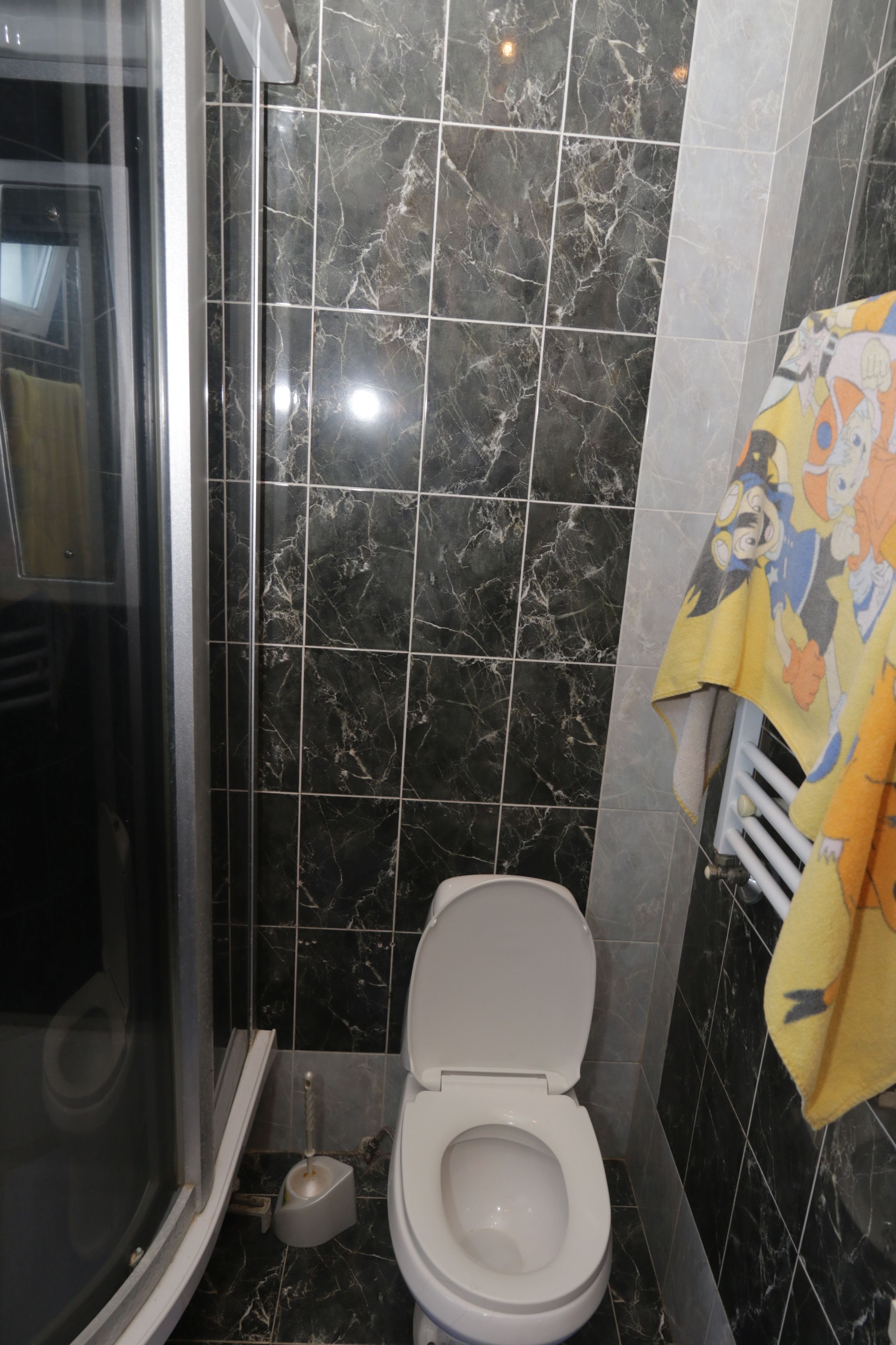Un baño con ducha, inodoro y un perchero con una toalla de caricatura.