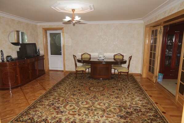 A dining room with a wooden table, chairs, and a patterned rug.