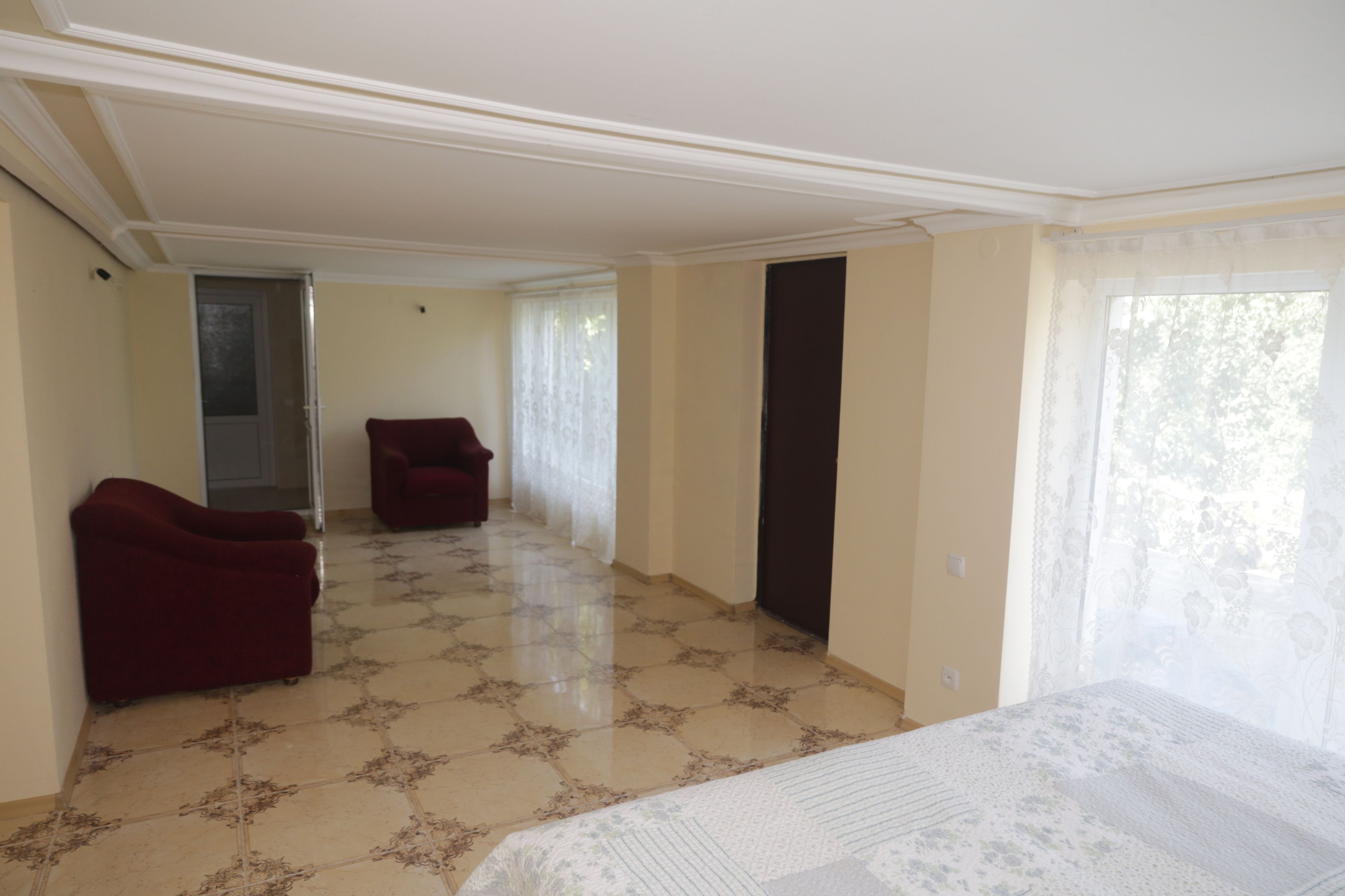 Una habitación amplia con una cama grande, dos sillones rojos y una puerta que da a otra estancia.