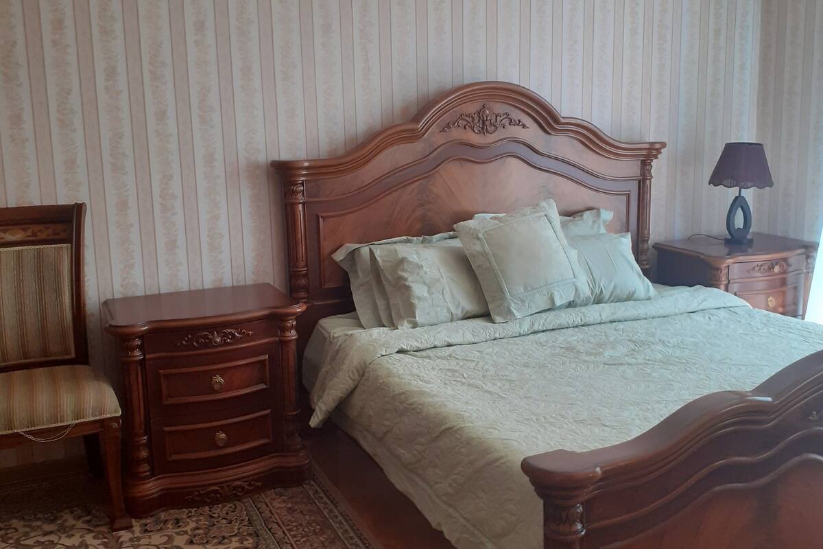 A bedroom with a wooden bed, a nightstand, a chair, and a patterned rug.
