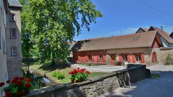 A traditional building with a stone facade, a red-tiled roof, and a small pond with red flowers in the foreground.