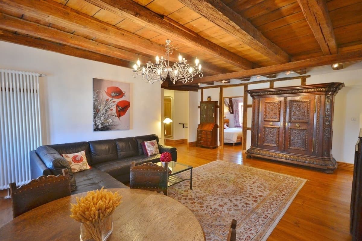 A living room with a wooden ceiling, a black leather sofa, a glass coffee table, and a large wooden cabinet.