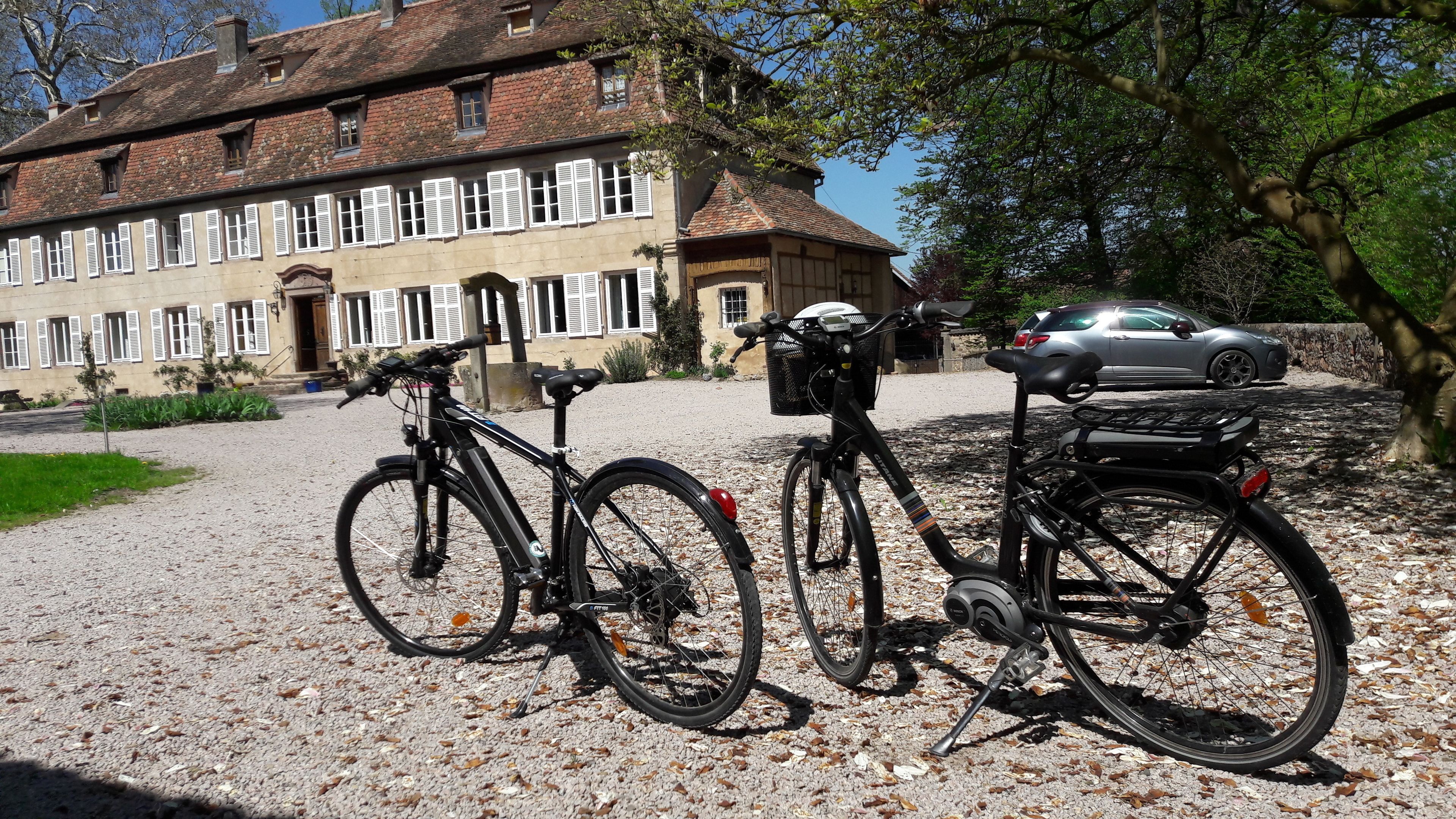 Two bicycles parked on a gravel driveway with a building in the background.