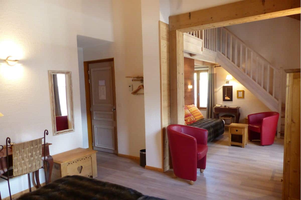 Un salon chaleureux avec un escalier en bois, un canapé, un fauteuil rouge et une petite table.