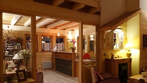A cozy wooden interior with a fireplace, wicker furniture, and a bookshelf. - Hotel Panoramic Village - La Grave (La Grave)