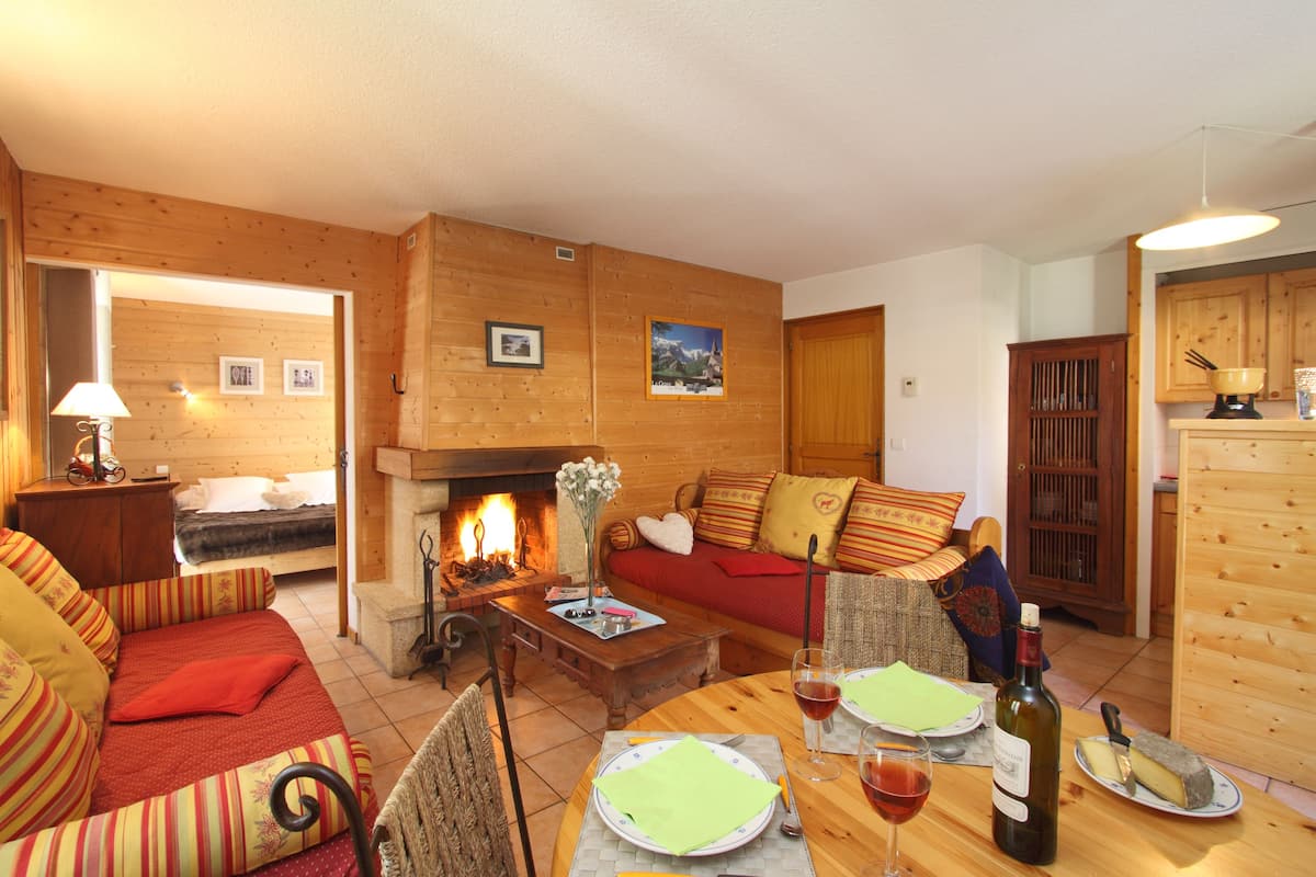 Un salon chaleureux avec une cheminée, des murs en bois, un canapé et une table à manger dressée pour deux personnes.