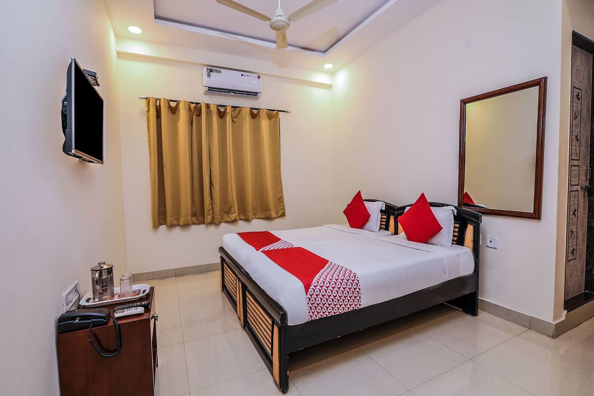 Habitación de hotel con cama, escritorio, teléfono, aire acondicionado y ventilador de techo, además de un espejo grande.
