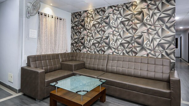 A modern living room with a geometric-patterned wall, a brown leather sofa, and a glass-top coffee table. - OYO 15928 Hotel Midtown (Hyderabad)