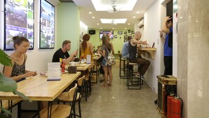 A dining area with tables and chairs, a menu stand, and a television screen displaying images. - Hanoi Amazing Hostel (Hanoi)