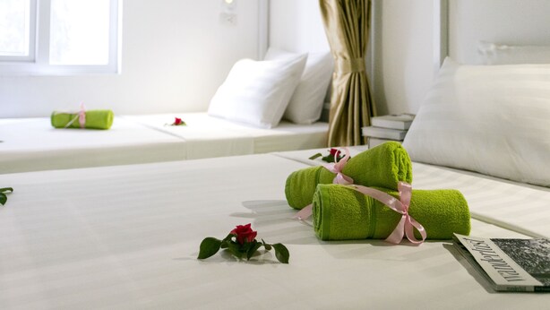 A neatly made bed with green towels, a rose, and a magazine on a white bedspread in a bright room with a window and curtains. - Hanoi Amazing Hostel (Hanoi)